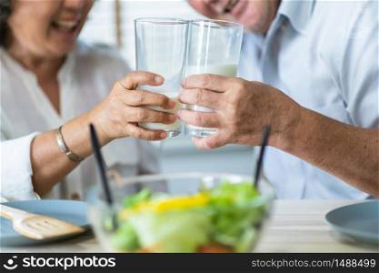 Healthy asian Elderly couple enjoying drinking fresh milk from glass. Happy Smiling Senior man and woman having fun with breakfast in the morning.