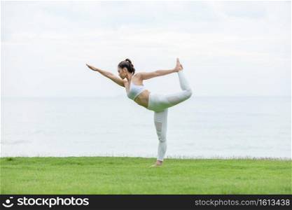 Healthy Asian woman wearing white shirt practicing yoga Standing bow pulling pose on the beach in thailand