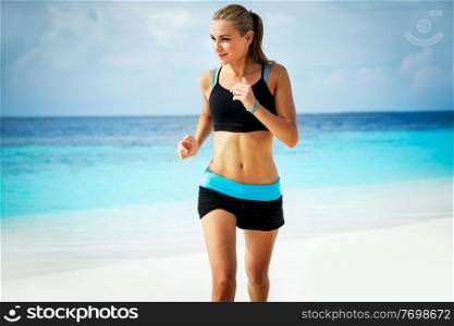 Healthy attractive woman jogging on the beautiful sandy beach, doing fitness exercise outdoors, enjoying workout near the sea, happy summer vacation