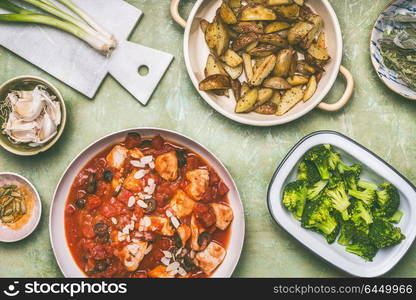 Healthy balanced eating concept. Pan with chicken pieces in tomatoes sauce, green cooked broccoli and baked potatoes on kitchen table background, top view