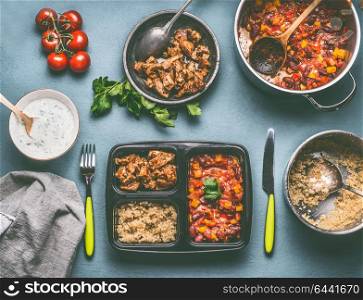 Healthy balanced lunch box preparation with quinoa, tomatoes beans sauce and chicken meat on kitchen table background with food pots and bowls, top view