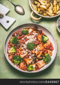 Healthy balanced meal. Pan with chicken pieces in tomatoes sauce, green broccoli and baked potatoes, top view