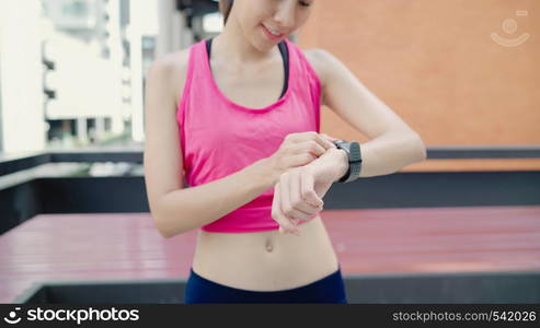 Healthy beautiful young Asian Athlete woman setting and checking progress looking heart rate monitor on smart watch while running in urban city. Lifestyle women exercise in the city concept.