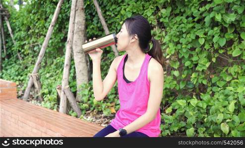 Healthy beautiful young Asian runner woman drinking water because feel tired after running on street in urban city park. Lifestyle fit and active women exercise in the city park concept.