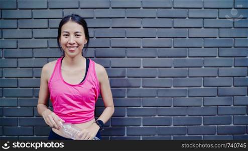 Healthy beautiful young Asian runner woman drinking water because feel tired after running on street in urban city. Lifestyle fit and active women exercise in the city concept.