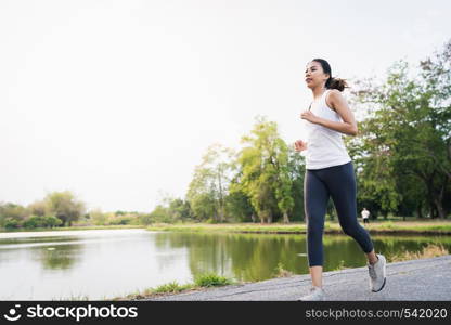 Healthy beautiful young Asian runner woman in sports clothing running and jogging on sidewalk near lake at park in the morning. Lifestyle fitness and active women exercise in urban city concept.