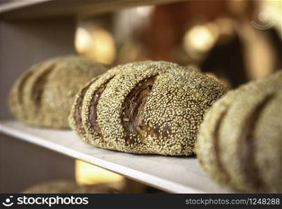 Healthy bread with golden crust and sesame seeds from sourdough on a wooden shelf. Freshly baked sesame bread on bakery shelf. Baker shop context.
