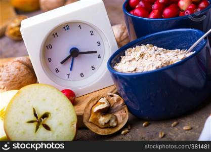 healthy breakfast - clock, milk, oatmeal, cranberries, nuts, apples on a wooden table