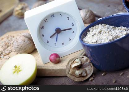 healthy breakfast - clock, milk, oatmeal, cranberries, nuts, apples on a wooden table