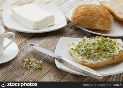 healthy breakfast concept - a roll with cream cheese and broccoli sprouts on a rustic wooden table