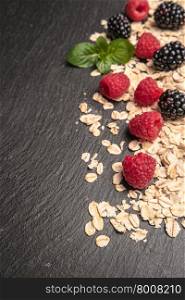 Healthy breakfast. Fresh granola, oatmeal with blackberries and raspberries on a black slate background. copy space