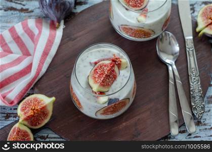 Healthy breakfast from natural ingredients .Homemade yogurt, slice of the fig, chia seeds and yogurt in glasses on the wooden background, top view.