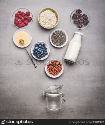 Healthy breakfast glass jar making with ingredients: chia seeds, goji berries, oatmeal , fresh berries , honey and milk or yogurt , top view, copy space