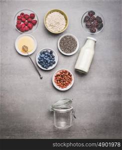Healthy breakfast glass jar making with ingredients: chia seeds, goji berries, oatmeal , fresh berries , honey and milk or yogurt , top view, copy space