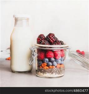 Healthy breakfast in glass making with oatmeal , Chia seeds, Goji berries, fresh berries and bottle of milk , front view, close up