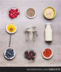 Healthy breakfast ingredients : honey, oatmeal , Chia seeds, Goji berries, fresh berries and bottle of milk with empty glass on gray background, top view, flat lay