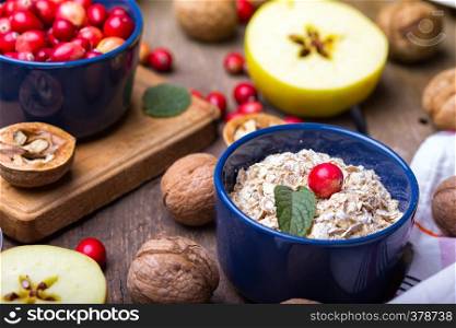 healthy breakfast - oatmeal, cranberries, nuts, apples on a wooden table