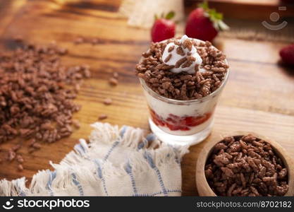 Healthy breakfast of Greek yogurt with fresh fruits and chocolate flavored puffed rice on a rustic wooden table.