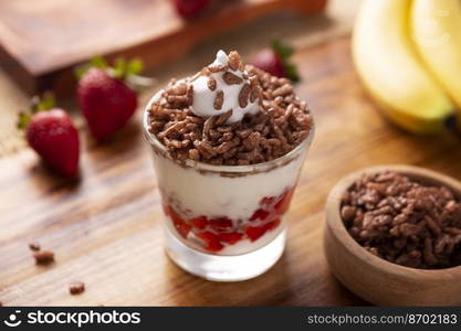 Healthy breakfast of Greek yogurt with fresh fruits and chocolate flavored puffed rice on a rustic wooden table.