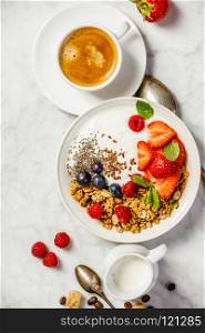 Healthy breakfast with coffee and Bowl of homemade granola with yogurt and fresh berries on white marble background. Top view, flat lay. Healthy breakfast with coffee, yogurt, granola and berries