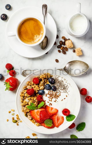 Healthy breakfast with coffee and Bowl of homemade granola with yogurt and fresh berries on white marble background. Top view, flat lay. Healthy breakfast with coffee, yogurt, granola and berries. Healthy breakfast with coffee, yogurt, granola and berries