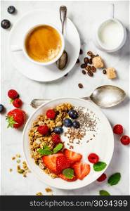 Healthy breakfast with coffee and Bowl of homemade granola with yogurt and fresh berries on white marble background. Top view, flat lay. Healthy breakfast with coffee, yogurt, granola and berries. Healthy breakfast with coffee, yogurt, granola and berries