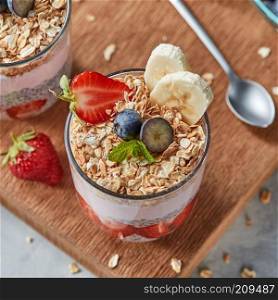 Healthy breakfast with homemde granola, yogurt, slices of strawberries, banana, blueberries, oat flaks, chia seeds on a wooden board. Concept of healthy dieting food.. The glass with oat flakes, banana fruits, strawberries, fresh smoothie, chia seeds on a wooden board.
