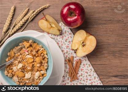 Healthy breakfast with muesli, red apple and cinnamon on rustic wooden table. Top view with copy space.