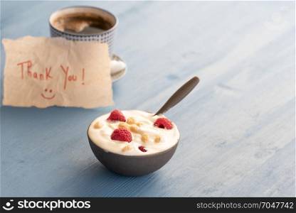 Healthy breakfast with yogurt and fresh raspberry fruits and a cup of coffee in background with a thank you message wrote on a piece of paper