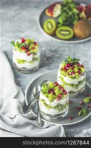 Healthy breakfast: yogurt parfait with granola and kiwi decoration pomegranate and mint on a gray background.
