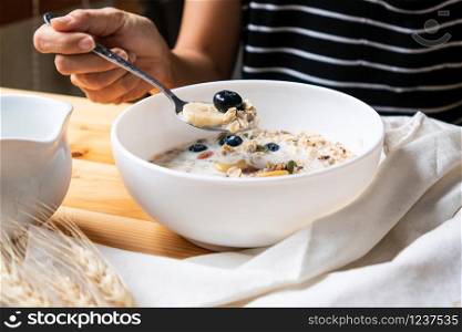 Healthy breakfast. Young Asian woman eating fresh granola, muesli with milk and berries on wooden table background.