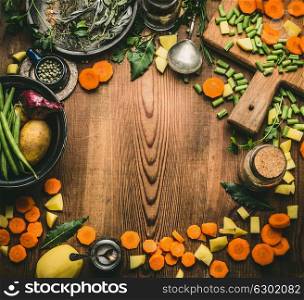 Healthy clean cooking and eating concept. Kitchen table from above with various ingredients: chopped vegetables, herbs and spices, cutting board and spoon, frame, top view