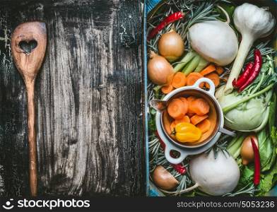 Healthy clean food background with various organic fresh vegetables in a crate and wooden cooking spoon with heart on dark rustic background, top view, frame. Vegetarian eating concept