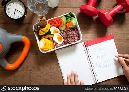 Healthy concept with nutrion food in lunch box and fitness equip. Healthy concept with nutrion food in lunch box and fitness equipments with woman writing time to get healthy on diary book