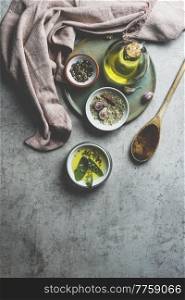 Healthy cooking ingredients on grey concrete kitchen table: olive oil, sage, garlic, pepper, salt, wooden cooking spoon, dish cloth. Cooking flavorful food at home. Top view.
