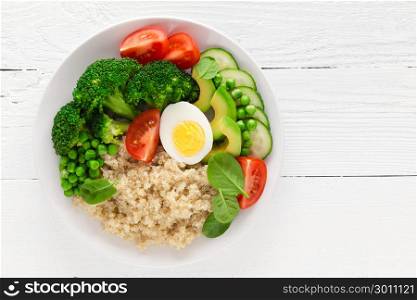 Healthy detox dish with egg, avocado, quinoa, spinach, fresh tomato, green peas and broccoli on white wooden background, top view