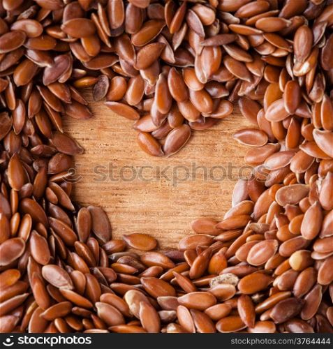 Healthy diet organic nutrition. Brown raw flax seeds linseed border frame with shapes heart sign on wooden table background