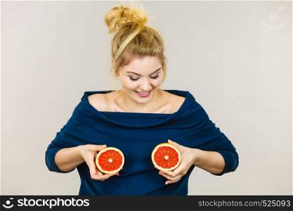 Healthy diet, refreshing food full of vitamins. Happy crazy woman holding sweet delicious citrus fruit, red grapefruit on breast. Woman holding red grapefruit on breast