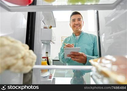 healthy eating and diet concept - smiling middle-aged man opening fridge and making list of necessary food at home kitchen. man making list of necessary food at home fridge