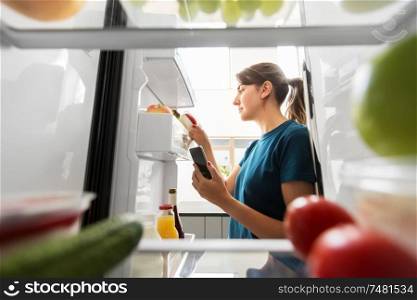 healthy eating and diet concept - woman at fridge with smartphone making list of necessary food at home kitchen. woman with smartphone makes list of food in fridge