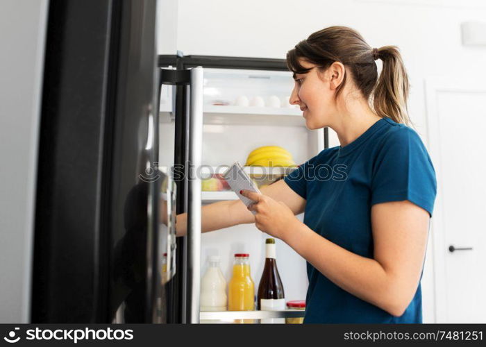 healthy eating and diet concept - woman opening fridge and making list of necessary food at home kitchen. woman making list of necessary food at home fridge