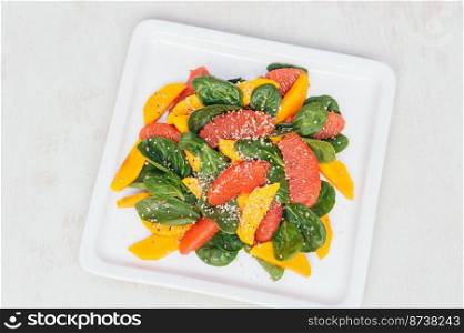 Healthy eating and dieting concept. Fresh salad of mango, grapefruit, spinach and hempseed on white square plate. Top view. Organic dish