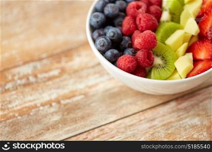 healthy eating and food concept - close up of fruits and berries in bowl on wooden table. close up of fruits and berries in bowl