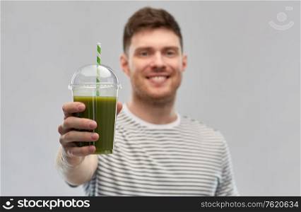 healthy eating and people concept - happy smiling man drinking green smoothie from disposable plastic cup with paper straw on grey background. man drinking green smoothie from disposable cup
