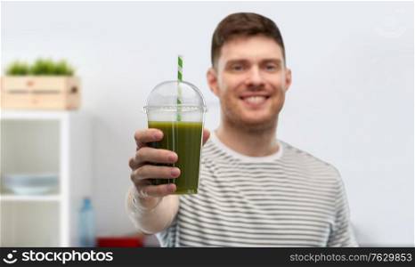 healthy eating and people concept - happy smiling man drinking green smoothie from disposable plastic cup with paper straw over home kitchen background. man drinking green smoothie from disposable cup