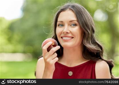 healthy eating and people concept - portrait of happy woman with peach at summer park. happy woman eating peach at summer park
