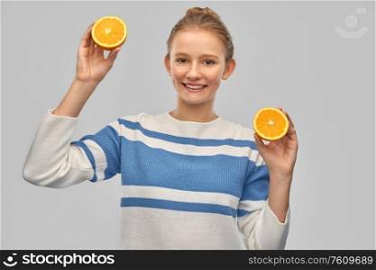 healthy eating and people concept - smiling teenage girl in pullover with orange halves over grey background. smiling teenage girl in pullover with oranges