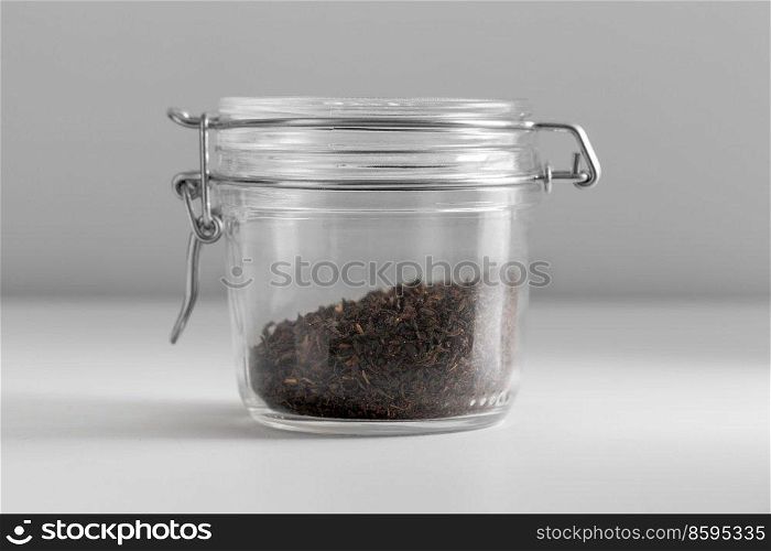 healthy eating and storage concept - jar with black tea on white background. close up of jar with black tea on white table