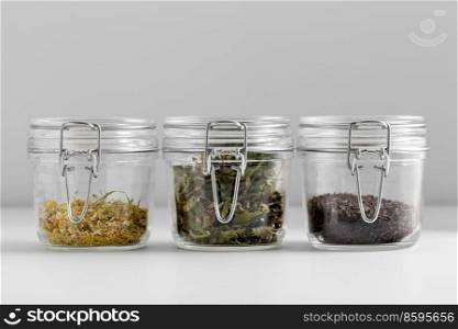 healthy eating and storage concept - jars with dried herbs on white background. close up of jars with dried herbs on white table
