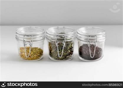 healthy eating and storage concept - jars with dried herbs on white table. close up of jars with dried herbs on white table